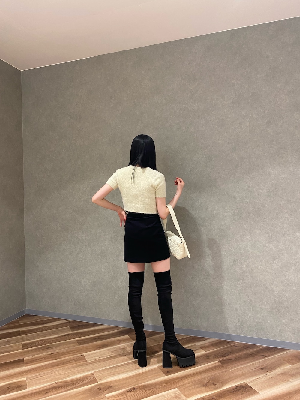 ブラック系のスカート、ホワイト系のハンドバッグ、ブラック系のブーツを着用したレディースの夏コーディネートの3枚目の写真