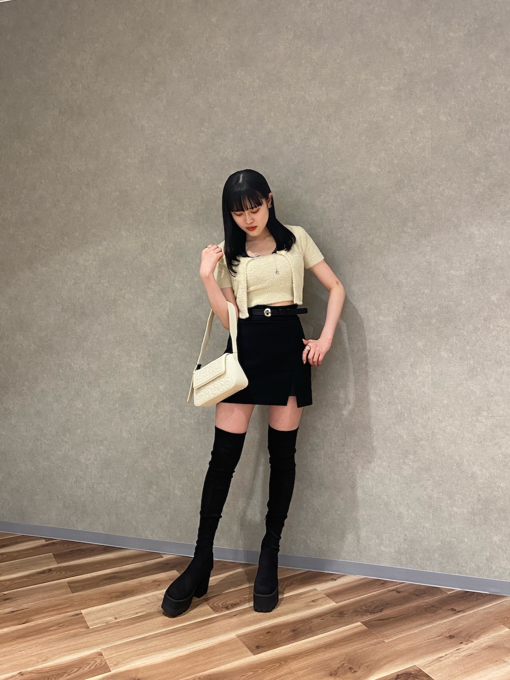 ブラック系のスカート、ホワイト系のハンドバッグ、ブラック系のブーツを着用したレディースの夏コーディネートの2枚目の写真