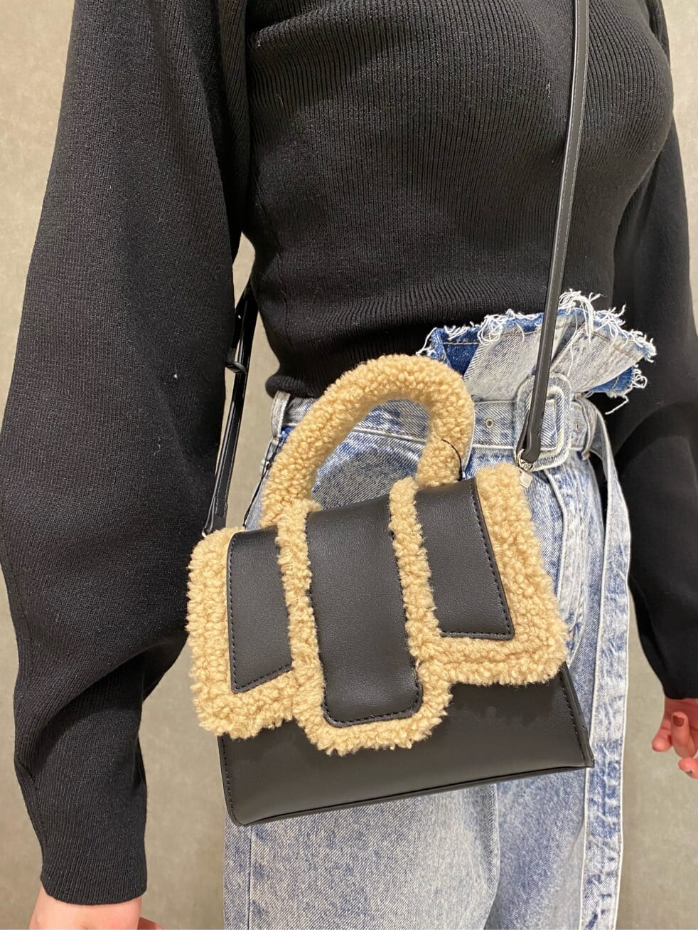 ブラック系のブーツ、ブラック系のハンドバッグ、ブルー系のデニムパンツを着用したレディースの秋コーディネートの4枚目の写真