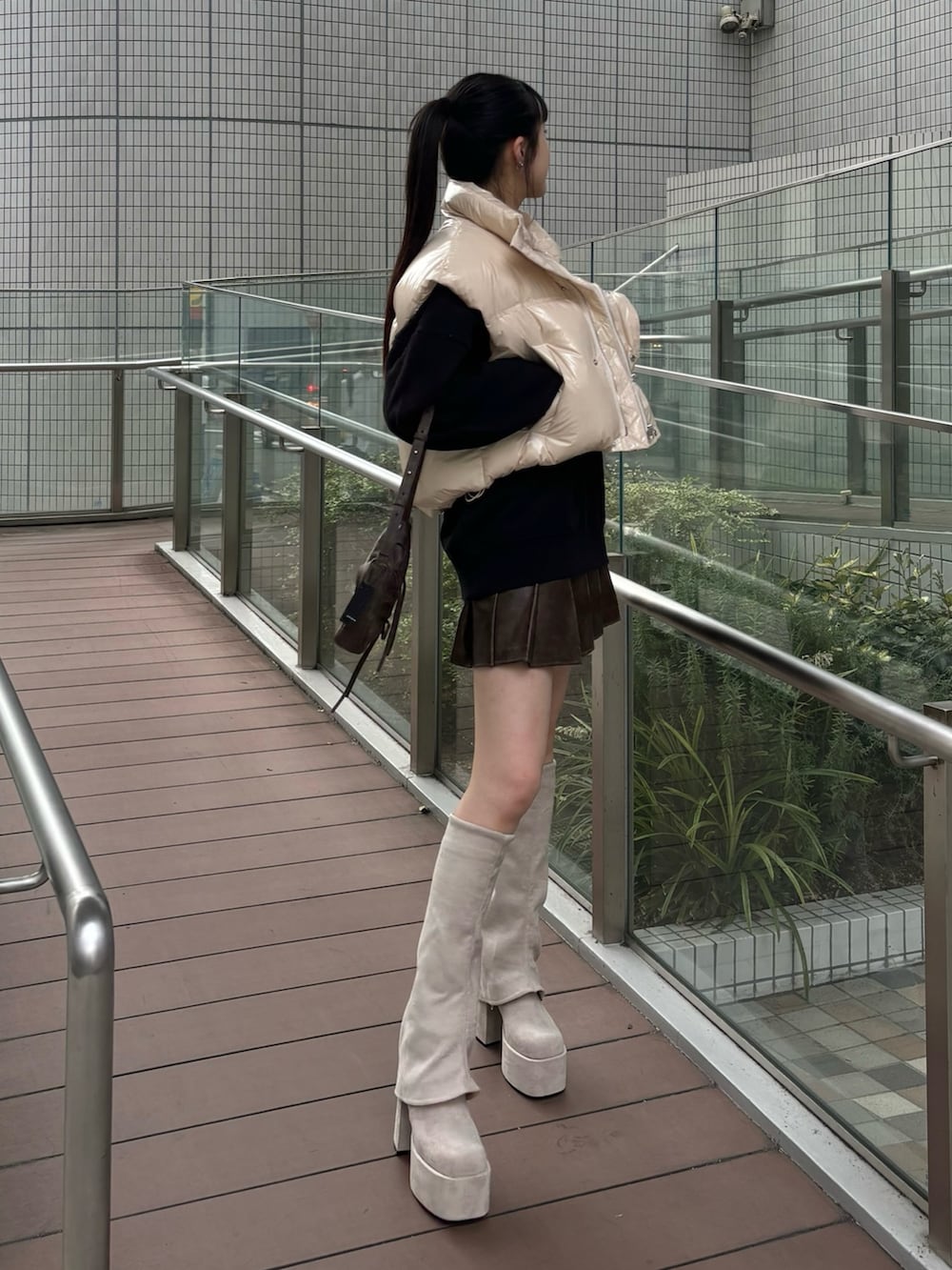 レッド系のショルダーバッグ、ホワイト系のダウンベスト、グレー系のスカートを着用したレディースの秋コーディネートの2枚目の写真