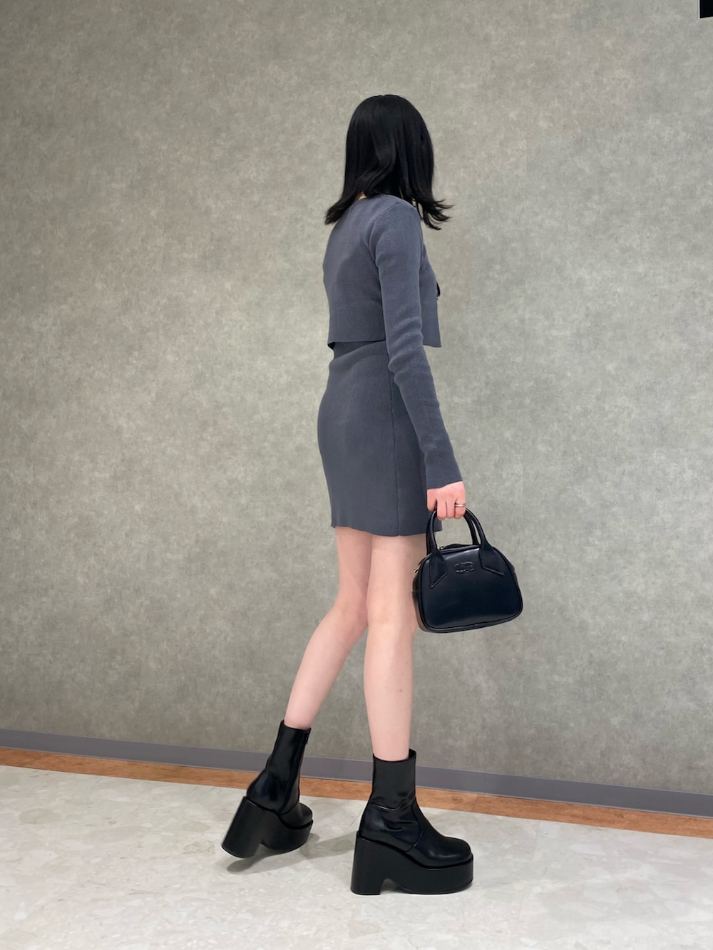 グレー系のワンピース、ブラック系のハンドバッグ、ブラック系のブーツを着用したレディースの春コーディネートの2枚目の写真