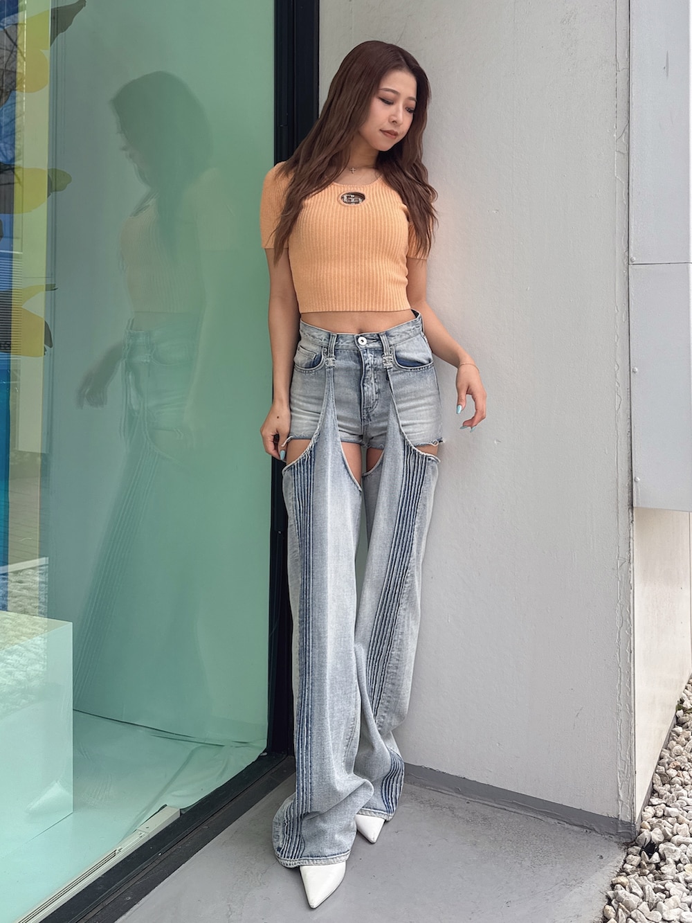 オレンジ系のニット/セーター、ブルー系のデニムパンツ、ホワイト系のパンプスを着用したレディースの春コーディネートの2枚目の写真