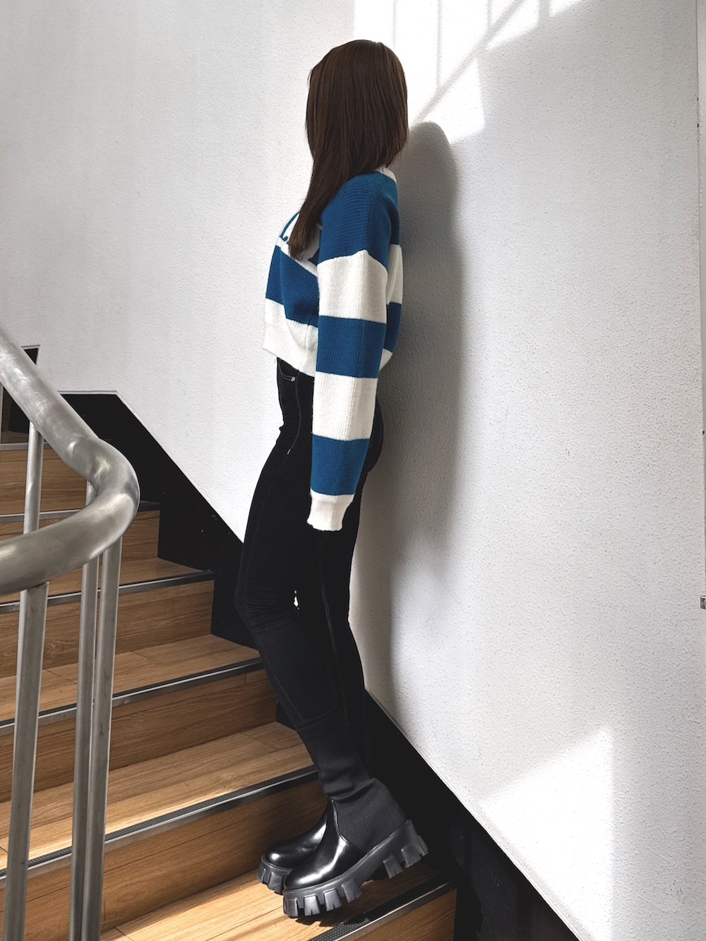 ブルー系のニット/セーター、ブラック系のデニムパンツ、ブラック系のブーツを着用したレディースの秋コーディネートの2枚目の写真