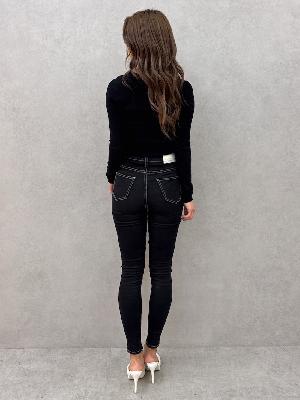 ブラック系のニット/セーター、ブラック系のデニムパンツ、ホワイト系のパンプスを着用したレディースの春コーディネートの4枚目の写真