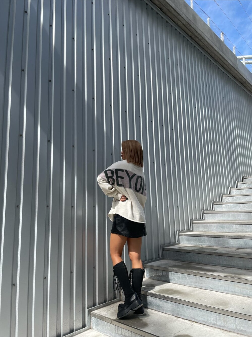 ブラック系のスカート、ブラック系のブーツ、ホワイト系のニット/セーターを着用したレディースの秋コーディネートの2枚目の写真