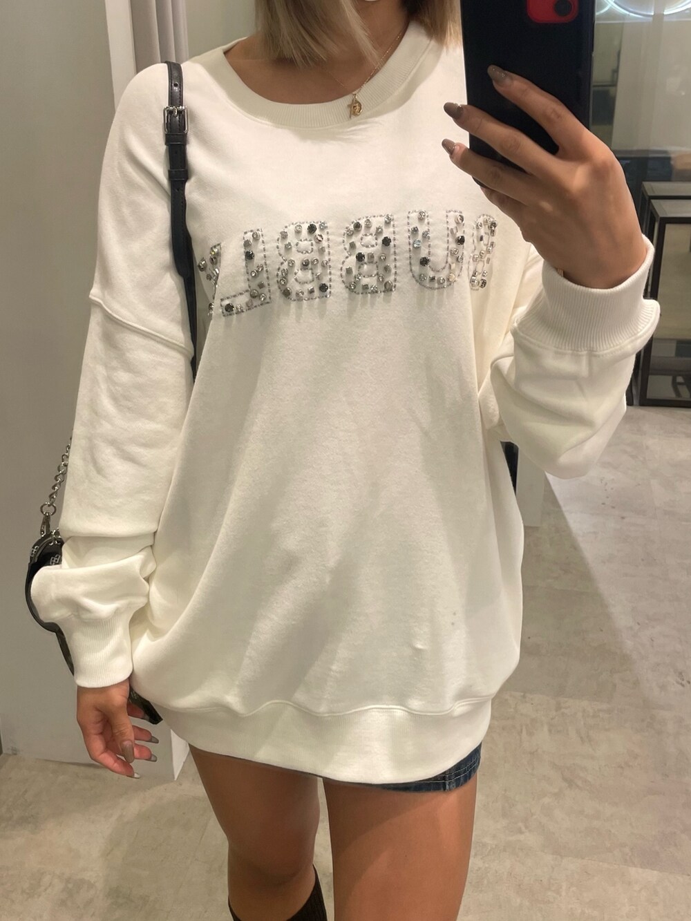 ホワイト系のスウェット、ブルー系のデニムスカート、ブラック系のショルダーバッグを着用したレディースの冬コーディネートの3枚目の写真