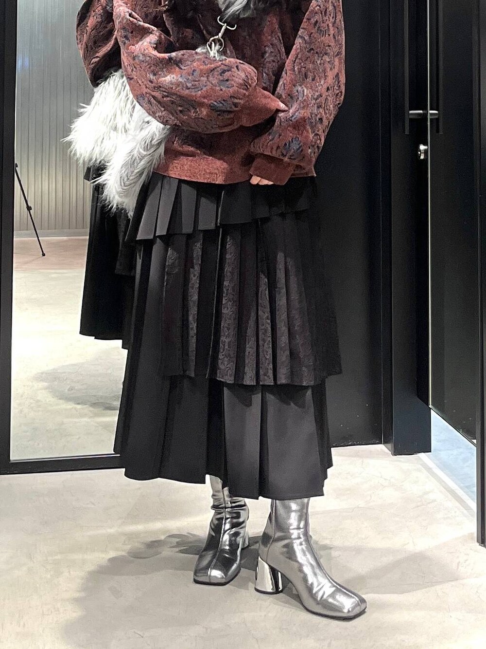 シルバー系のブーツ、レッド系のニット/セーター、ブラック系のスカートを着用したレディースの冬コーディネートの5枚目の写真