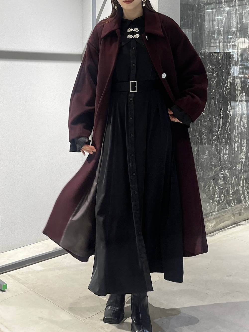 レッド系のステンカラーコート、ブラック系のブーツ、ブラック系のワンピースを着用したレディースの秋コーディネートの6枚目の写真