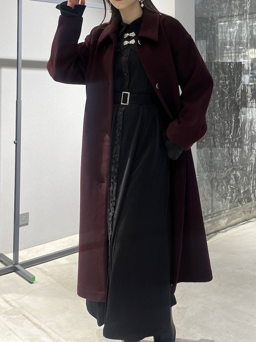 レッド系のステンカラーコート、ブラック系のブーツ、ブラック系のワンピースを着用したレディースの秋コーディネートの2枚目の写真