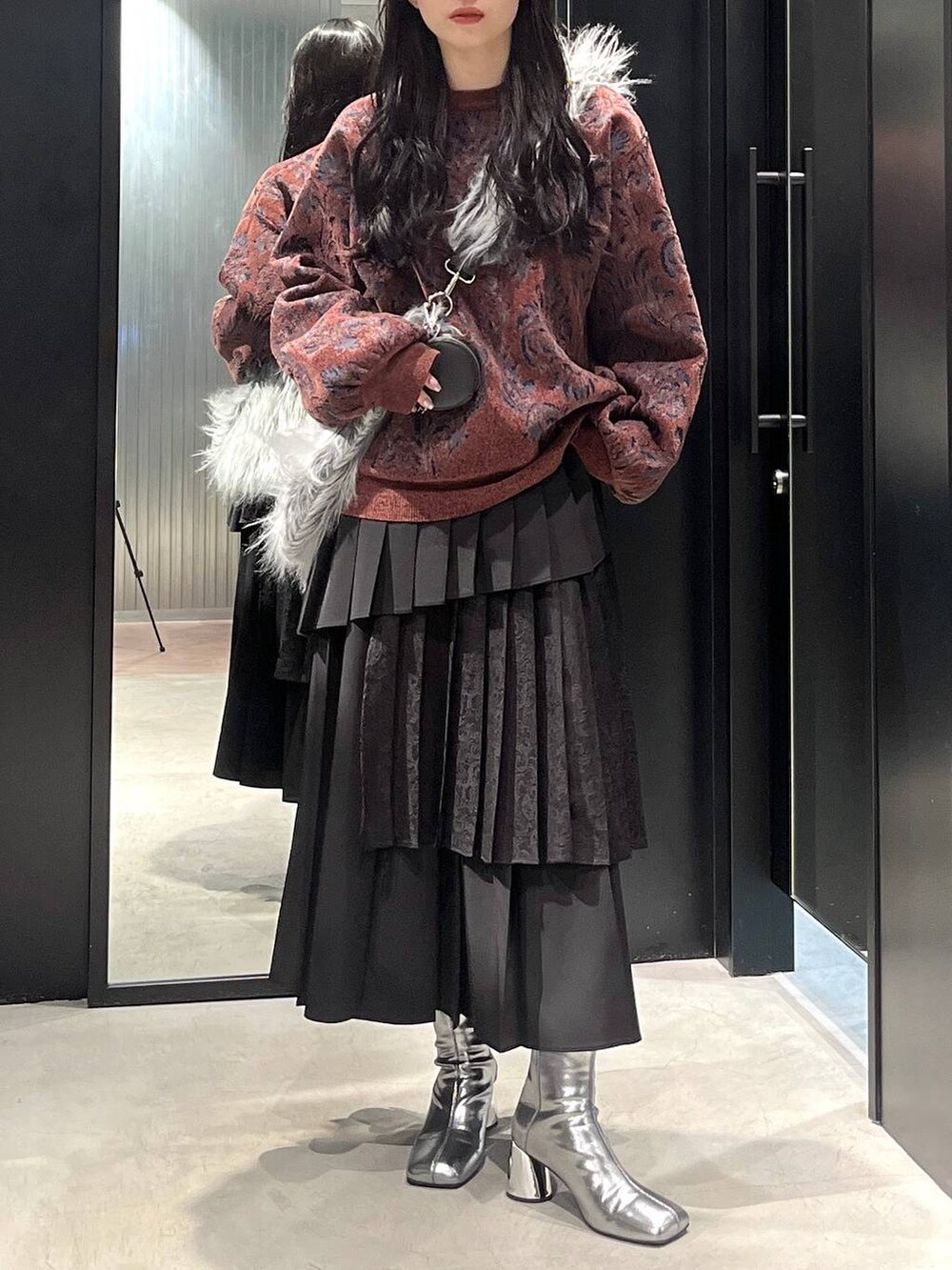 シルバー系のブーツ、レッド系のニット/セーター、ブラック系のスカートを着用したレディースの冬コーディネートの3枚目の写真