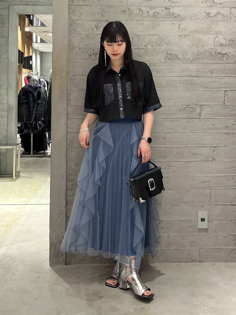 ブラック系のショルダーバッグ、ブルー系のスカート、シルバー系のサンダルを着用したレディースの春コーディネートの2枚目の写真