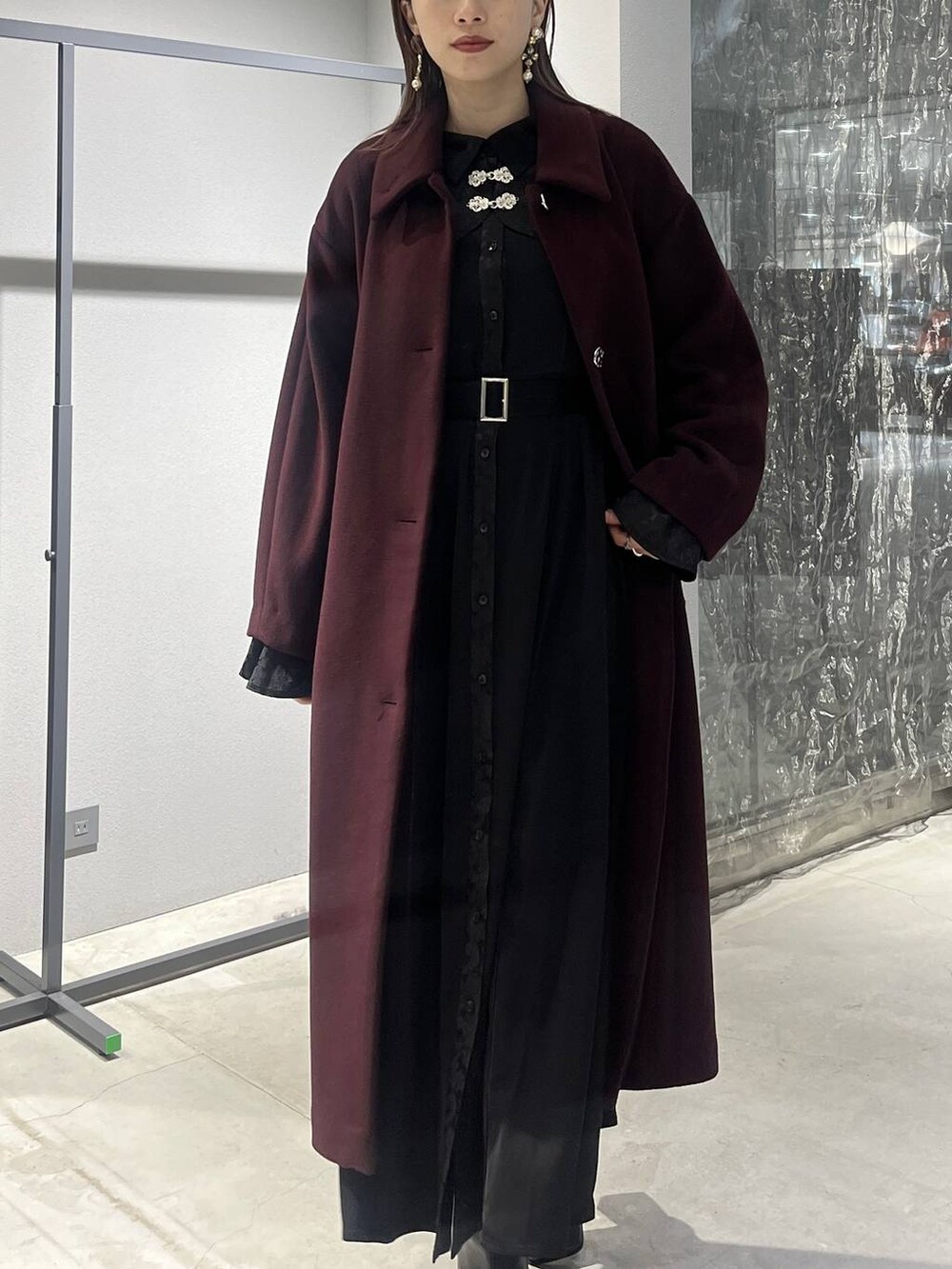 レッド系のステンカラーコート、ブラック系のブーツ、ブラック系のワンピースを着用したレディースの秋コーディネートの4枚目の写真