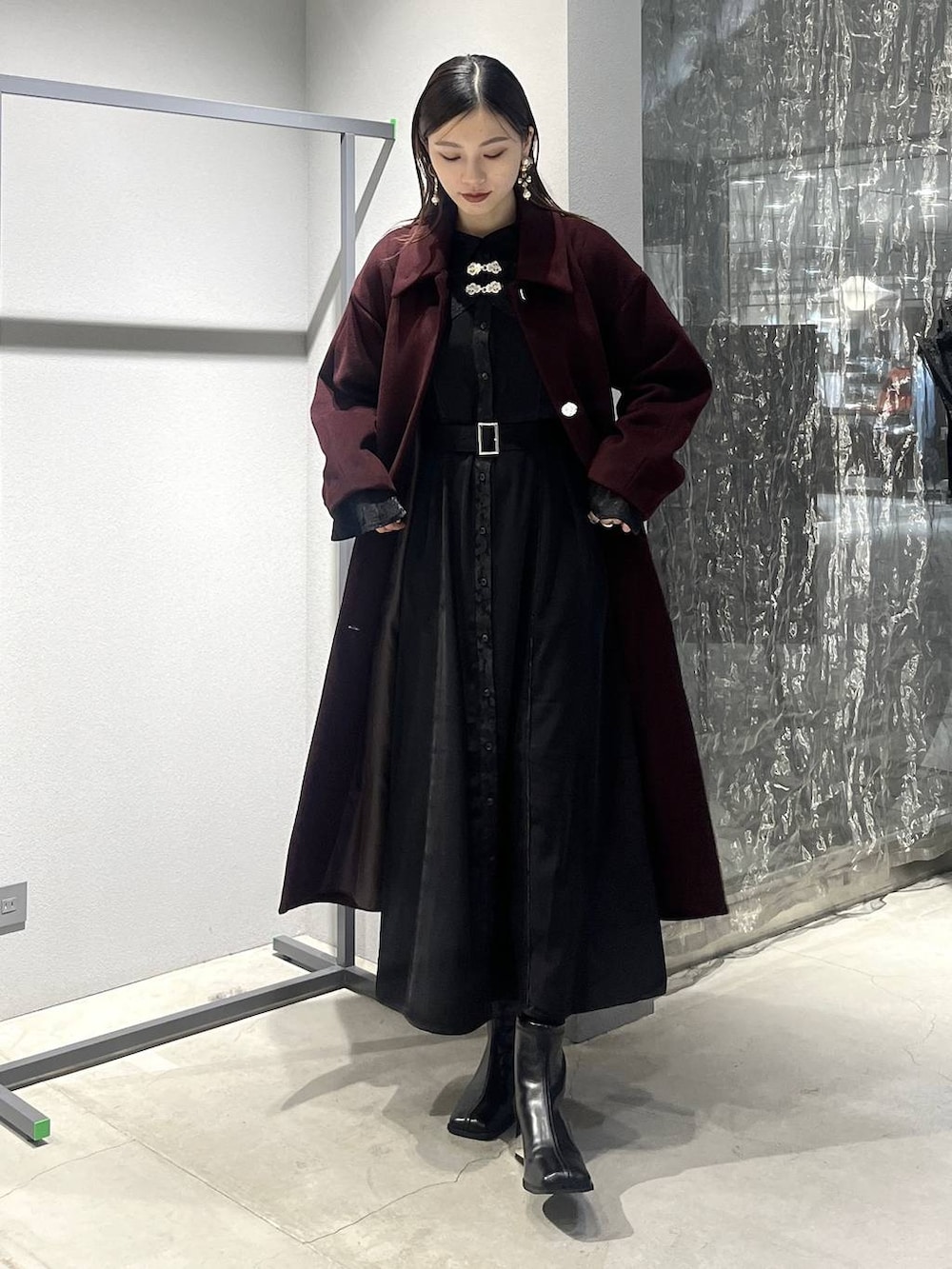 レッド系のステンカラーコート、ブラック系のブーツ、ブラック系のワンピースを着用したレディースの秋コーディネートの5枚目の写真