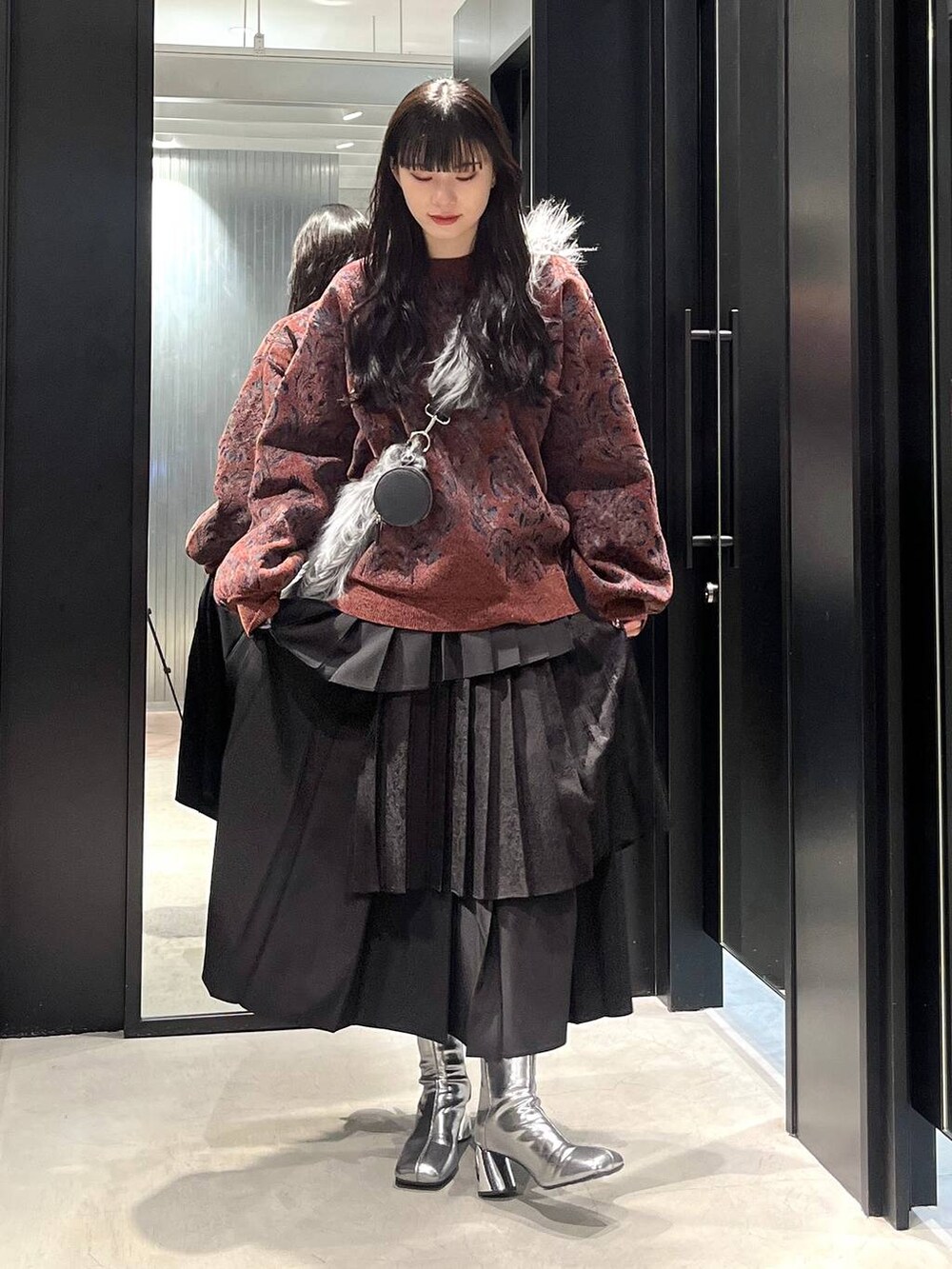 シルバー系のブーツ、レッド系のニット/セーター、ブラック系のスカートを着用したレディースの冬コーディネートの2枚目の写真