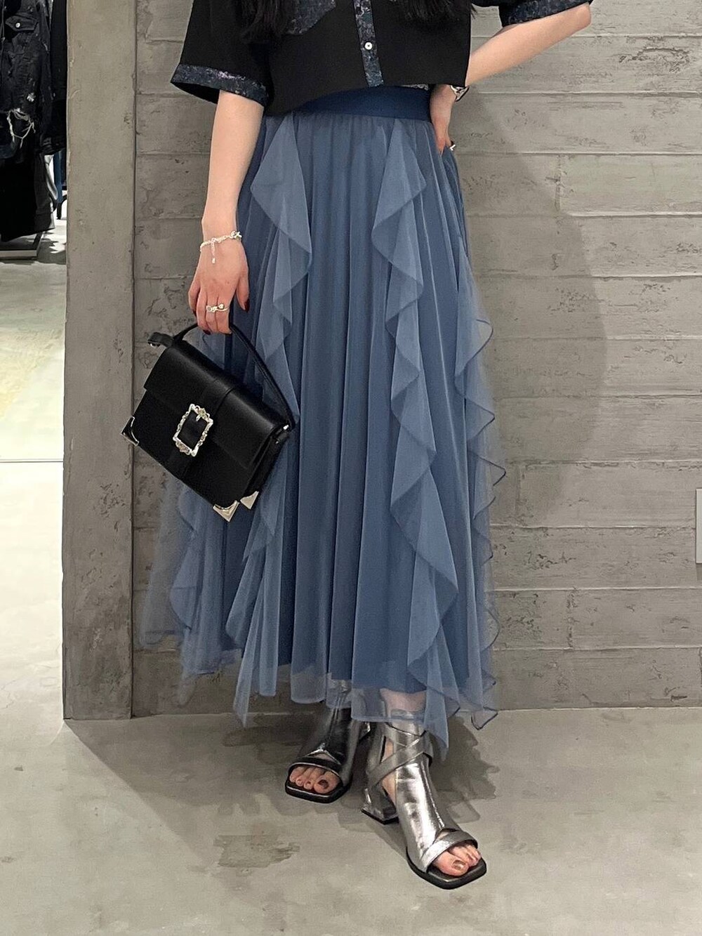 ブラック系のショルダーバッグ、ブルー系のスカート、シルバー系のサンダルを着用したレディースの春コーディネートの3枚目の写真