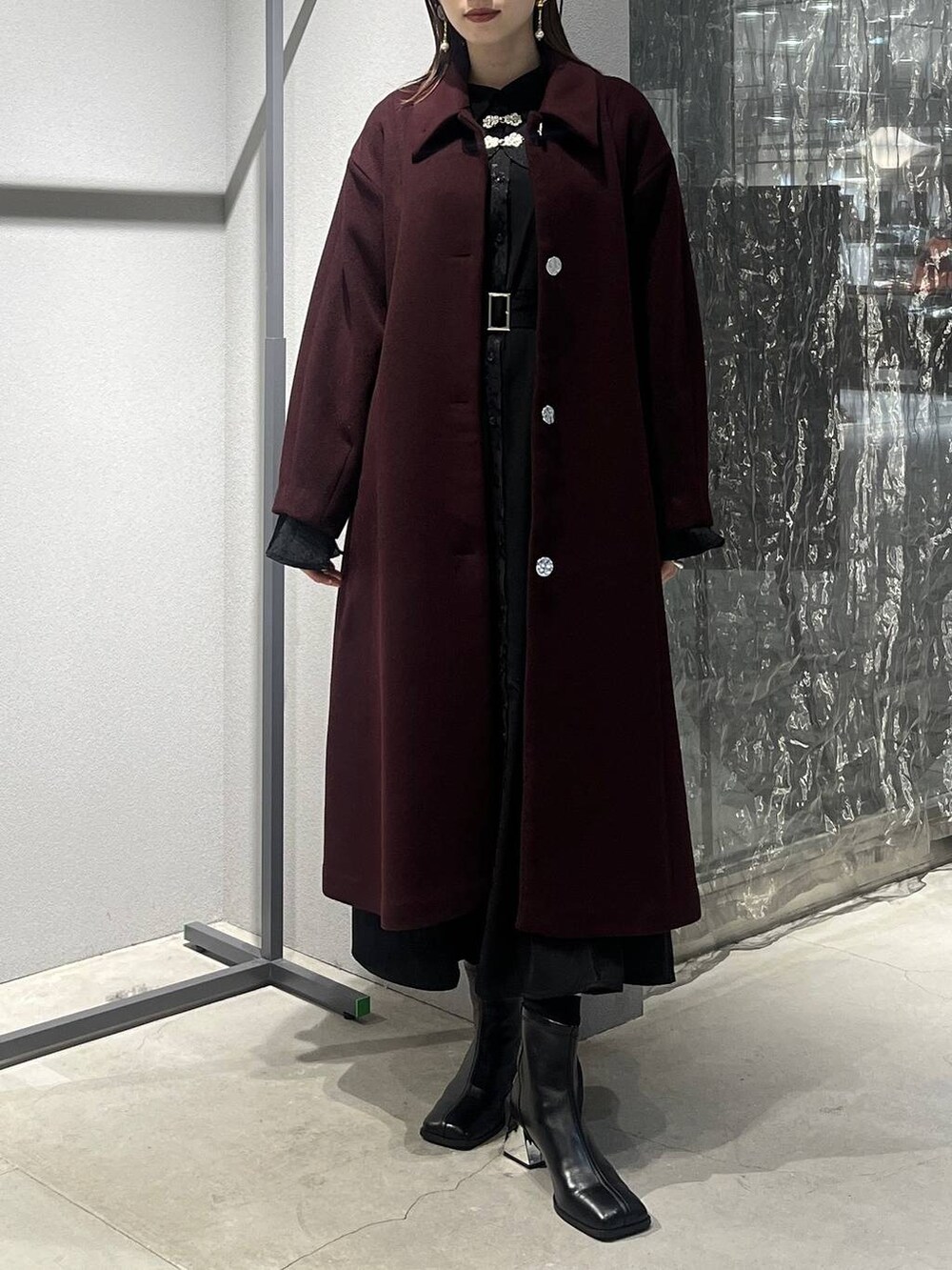 レッド系のステンカラーコート、ブラック系のブーツ、ブラック系のワンピースを着用したレディースの秋コーディネートの3枚目の写真