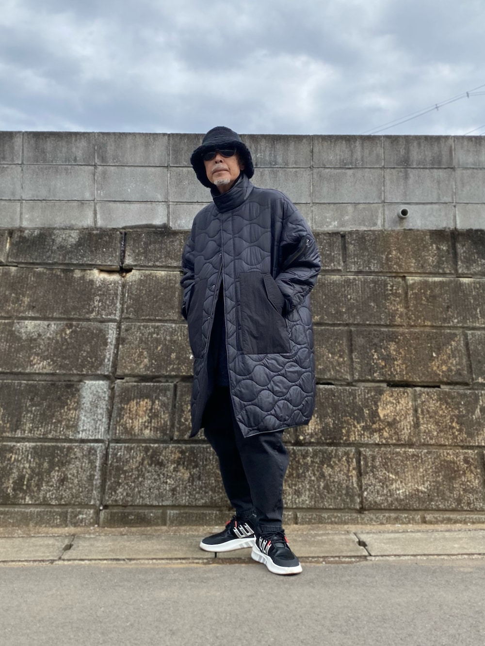 ブラック系のノーカラーコート、ブラック系のデニムパンツ、ブラック系のスニーカーを着用したメンズの春コーディネートの4枚目の写真