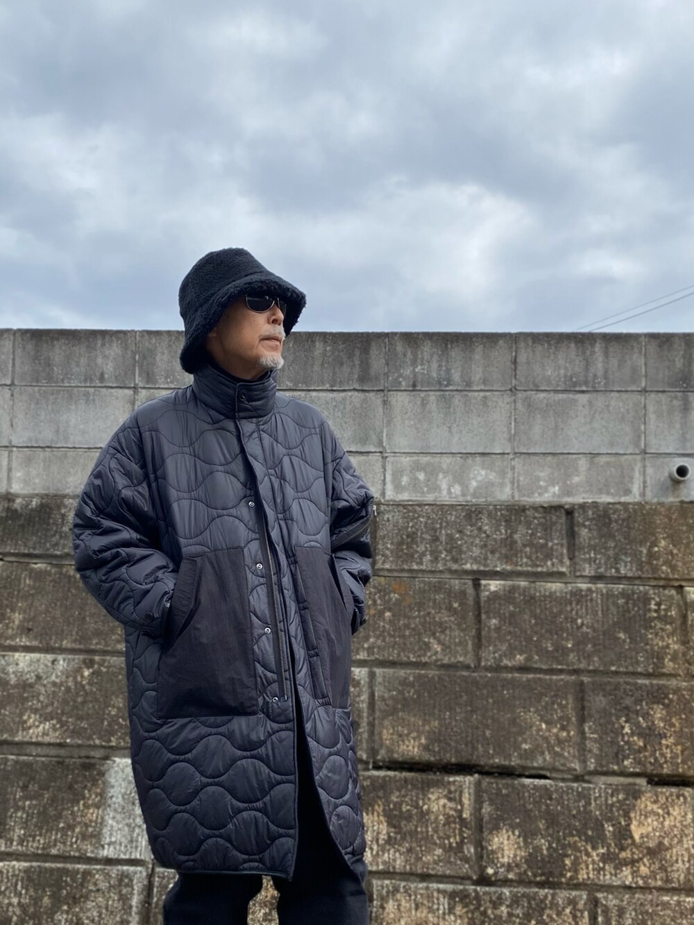 ブラック系のノーカラーコート、ブラック系のデニムパンツ、ブラック系のスニーカーを着用したメンズの春コーディネートの3枚目の写真