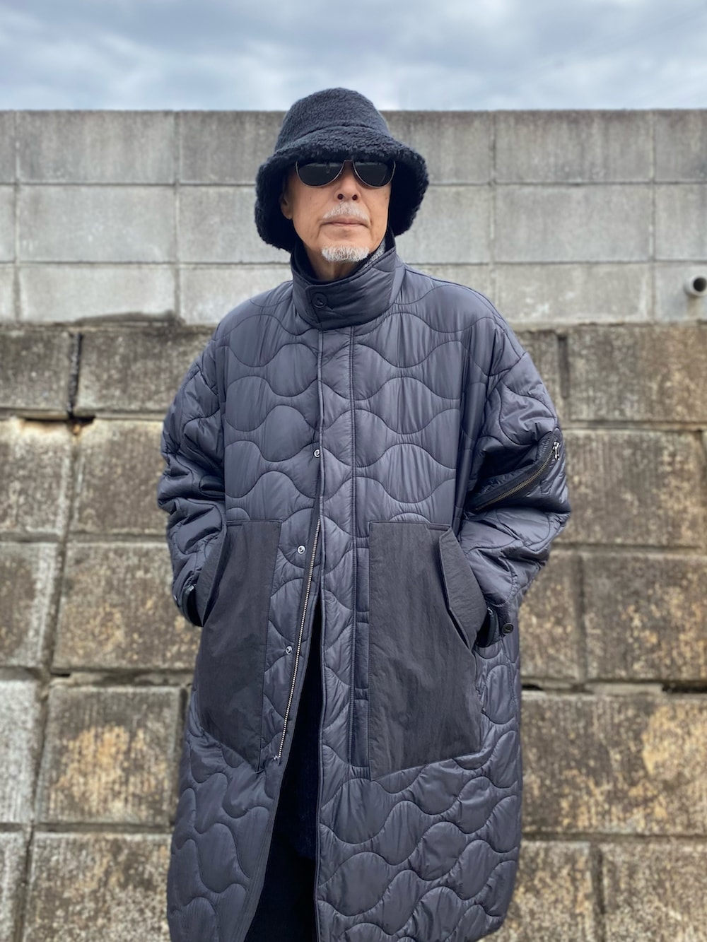 ブラック系のノーカラーコート、ブラック系のデニムパンツ、ブラック系のスニーカーを着用したメンズの春コーディネートの2枚目の写真