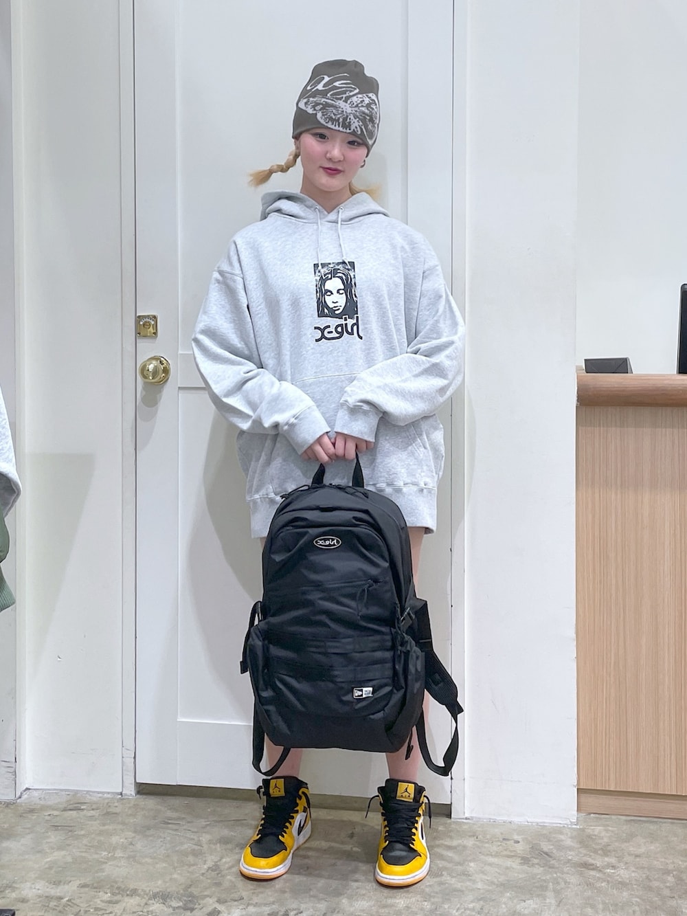 グレー系のパーカー、ブラック系のバックパック/リュック、グリーン系のニットキャップ/ビーニーを着用したレディースの春コーディネートの2枚目の写真