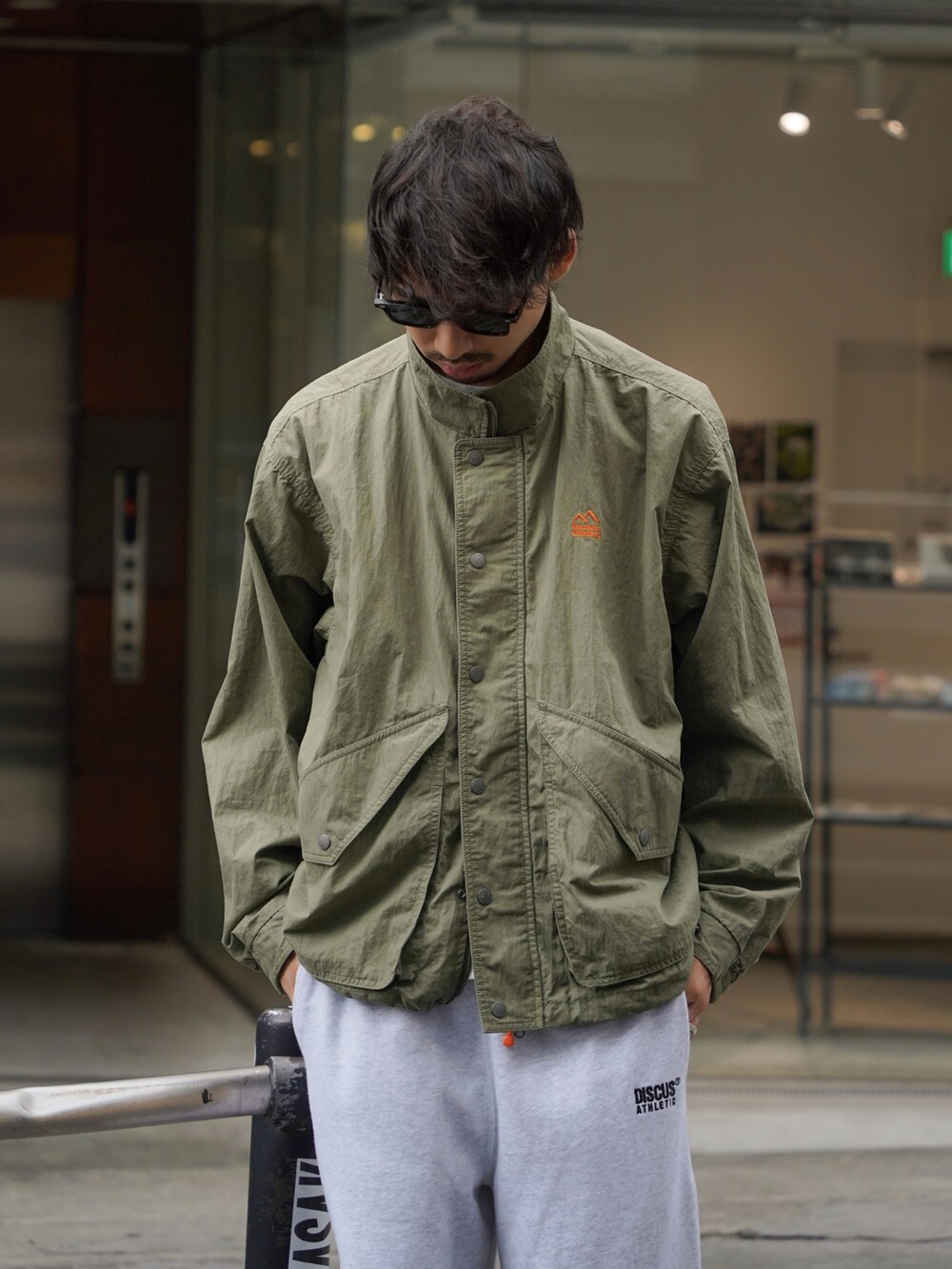 グレー系のスウェットパンツ、グリーン系のナイロンジャケットを着用したメンズの秋コーディネートの3枚目の写真