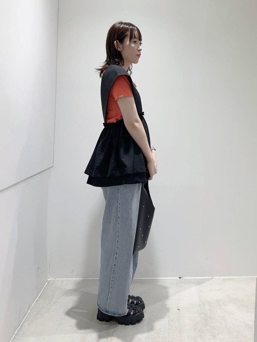 ブルー系のデニムパンツ、ブラック系のトートバッグ、オレンジ系のTシャツ/カットソーを着用したレディースの夏コーディネートの2枚目の写真