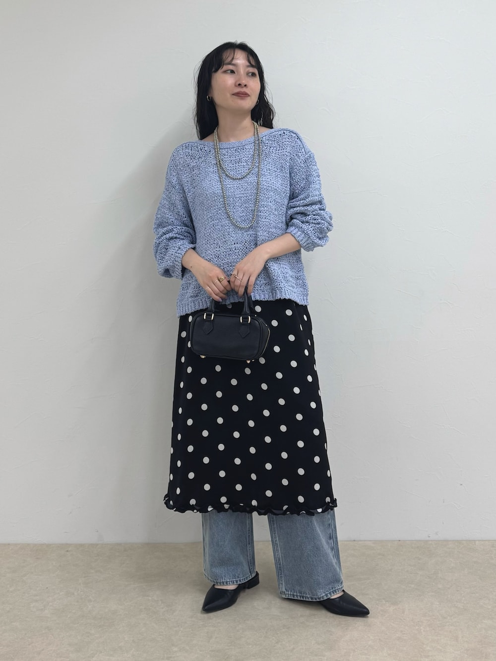 ブルー系のニット/セーター、ブラック系のスカート、ブルー系のデニムパンツを着用したレディースの春コーディネートの2枚目の写真