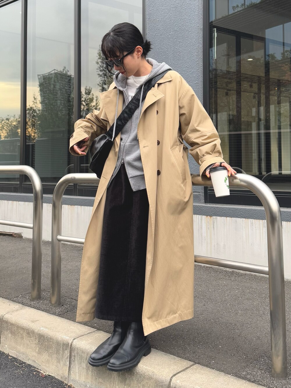 グレー系のパーカー、ベージュ系のトレンチコート、ブラック系のスカートを着用したレディースの冬コーディネートの4枚目の写真