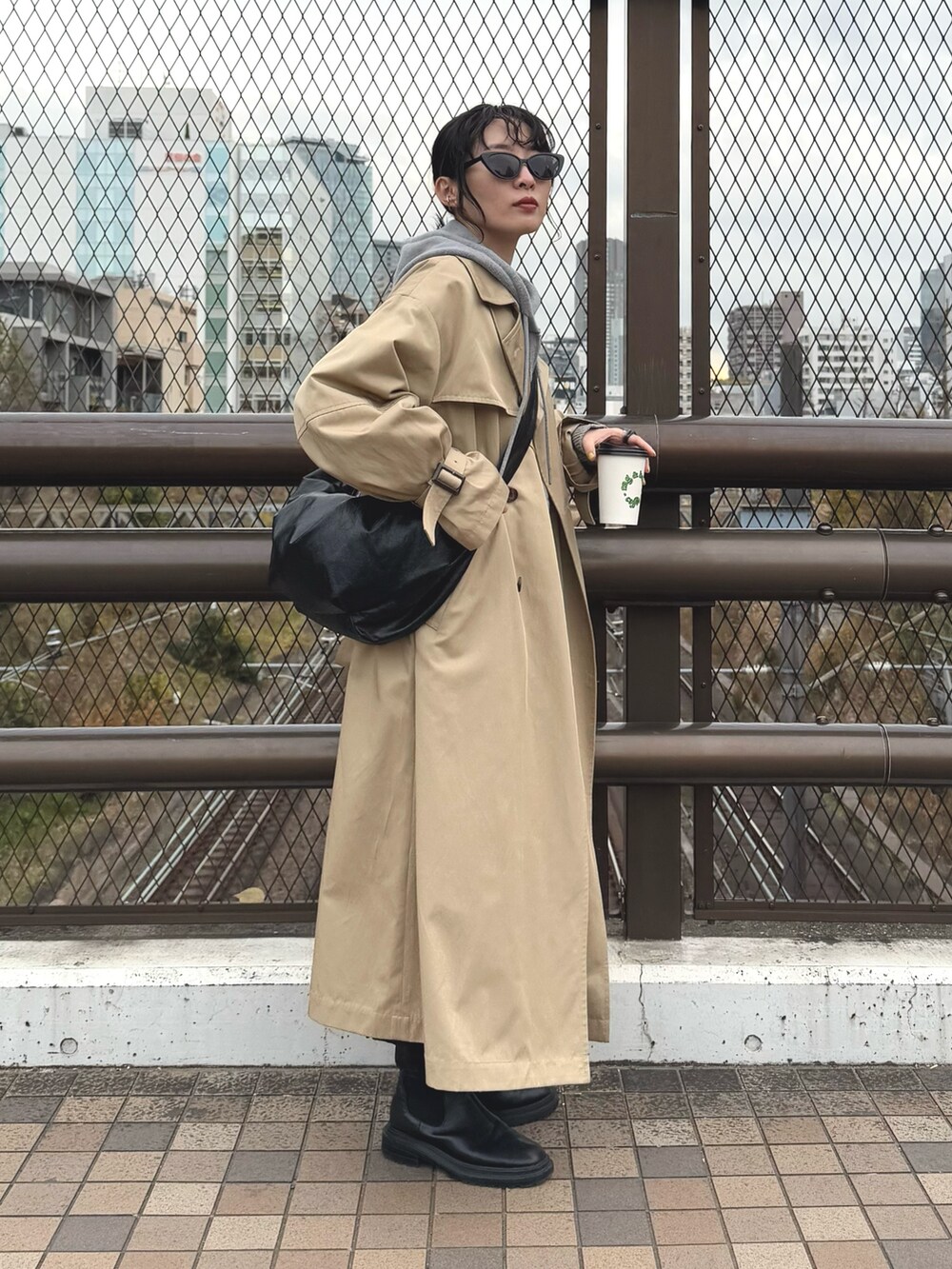 グレー系のパーカー、ベージュ系のトレンチコート、ブラック系のスカートを着用したレディースの冬コーディネートの2枚目の写真