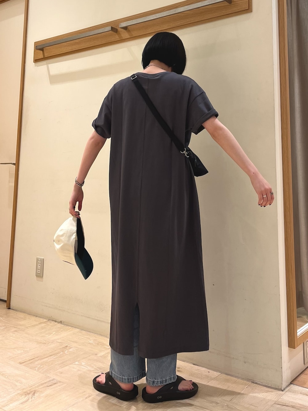 グレー系のワンピース、ブルー系のデニムパンツ、ブラック系のサンダルを着用したレディースの春コーディネートの2枚目の写真