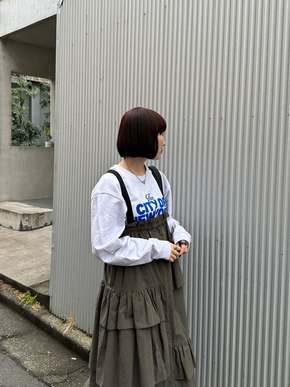 グレー系のスウェット、グリーン系のジャンパースカート、ブラック系のショルダーバッグを着用したレディースの冬コーディネートの4枚目の写真