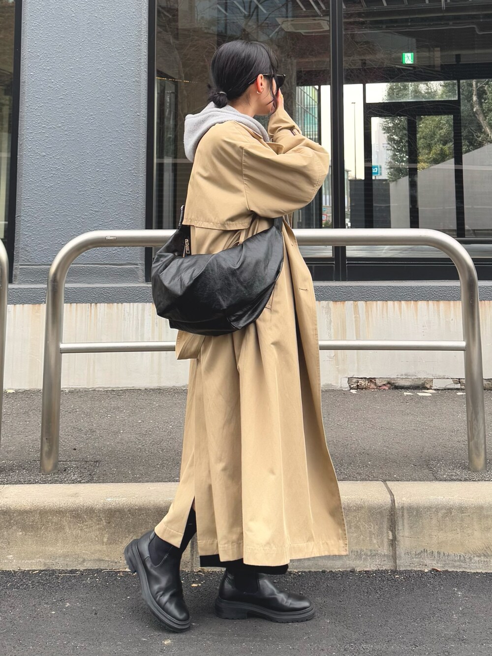 グレー系のパーカー、ベージュ系のトレンチコート、ブラック系のスカートを着用したレディースの冬コーディネートの6枚目の写真