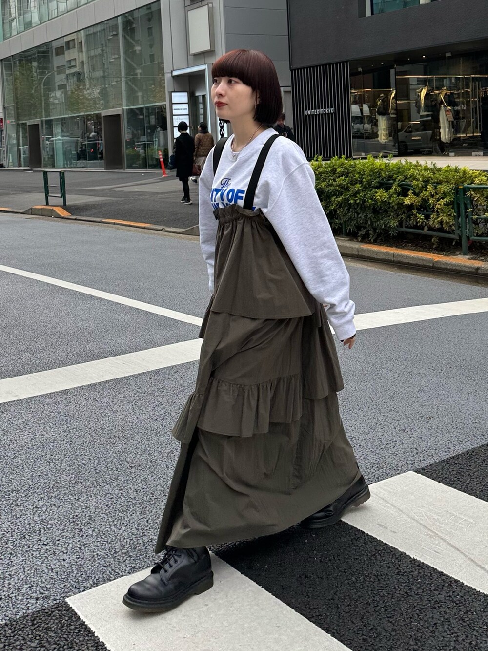 グレー系のスウェット、グリーン系のジャンパースカート、ブラック系のショルダーバッグを着用したレディースの冬コーディネートの2枚目の写真