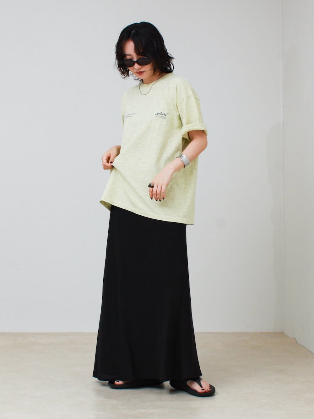 イエロー系のTシャツ/カットソー、ブラック系のスカート、ブラック系のサンダルを着用したレディースの夏コーディネートの3枚目の写真