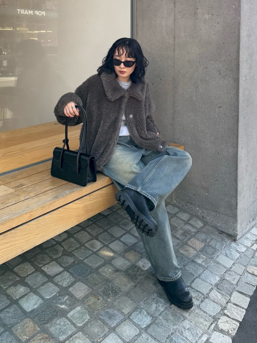 グレー系のムートンコート、グレー系のニット/セーター、ブラック系のハンドバッグを着用したレディースの冬コーディネートの3枚目の写真
