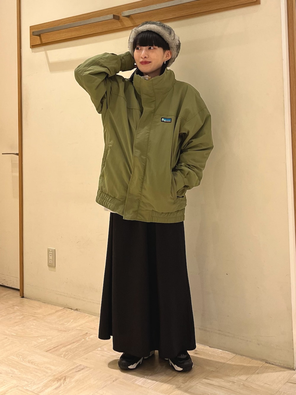 グリーン系のナイロンジャケット、ブラック系のスカート、ブラック系のキャップを着用したレディースの秋コーディネートの2枚目の写真