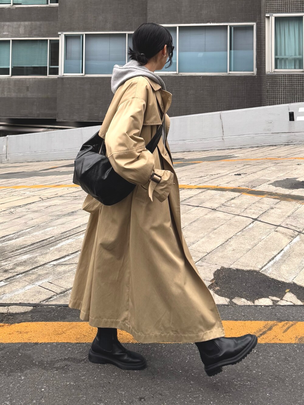 グレー系のパーカー、ベージュ系のトレンチコート、ブラック系のスカートを着用したレディースの冬コーディネートの3枚目の写真