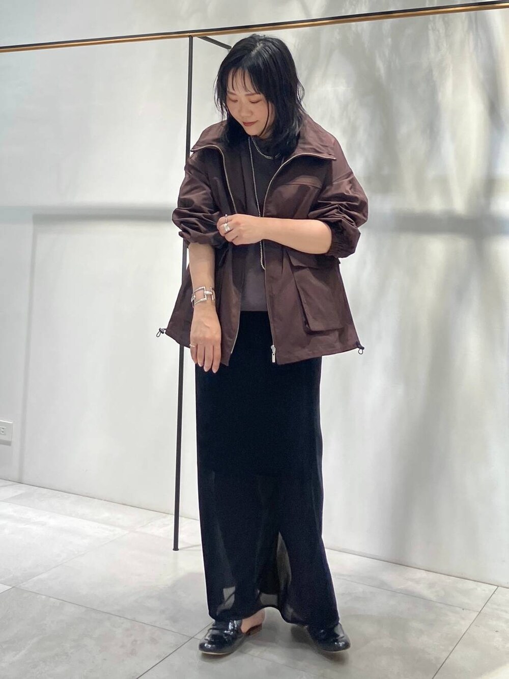 ブラック系のスカート、ブラウン系のTシャツ/カットソー、ブラウン系のブルゾンを着用したレディースの夏コーディネートの2枚目の写真