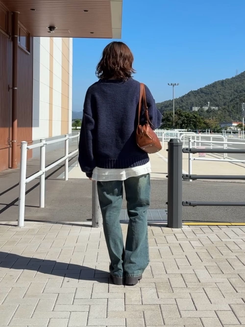 ブルー系のニット/セーター、ブルー系のデニムパンツ、ホワイト系のワンピースを着用したレディースの秋コーディネートの4枚目の写真