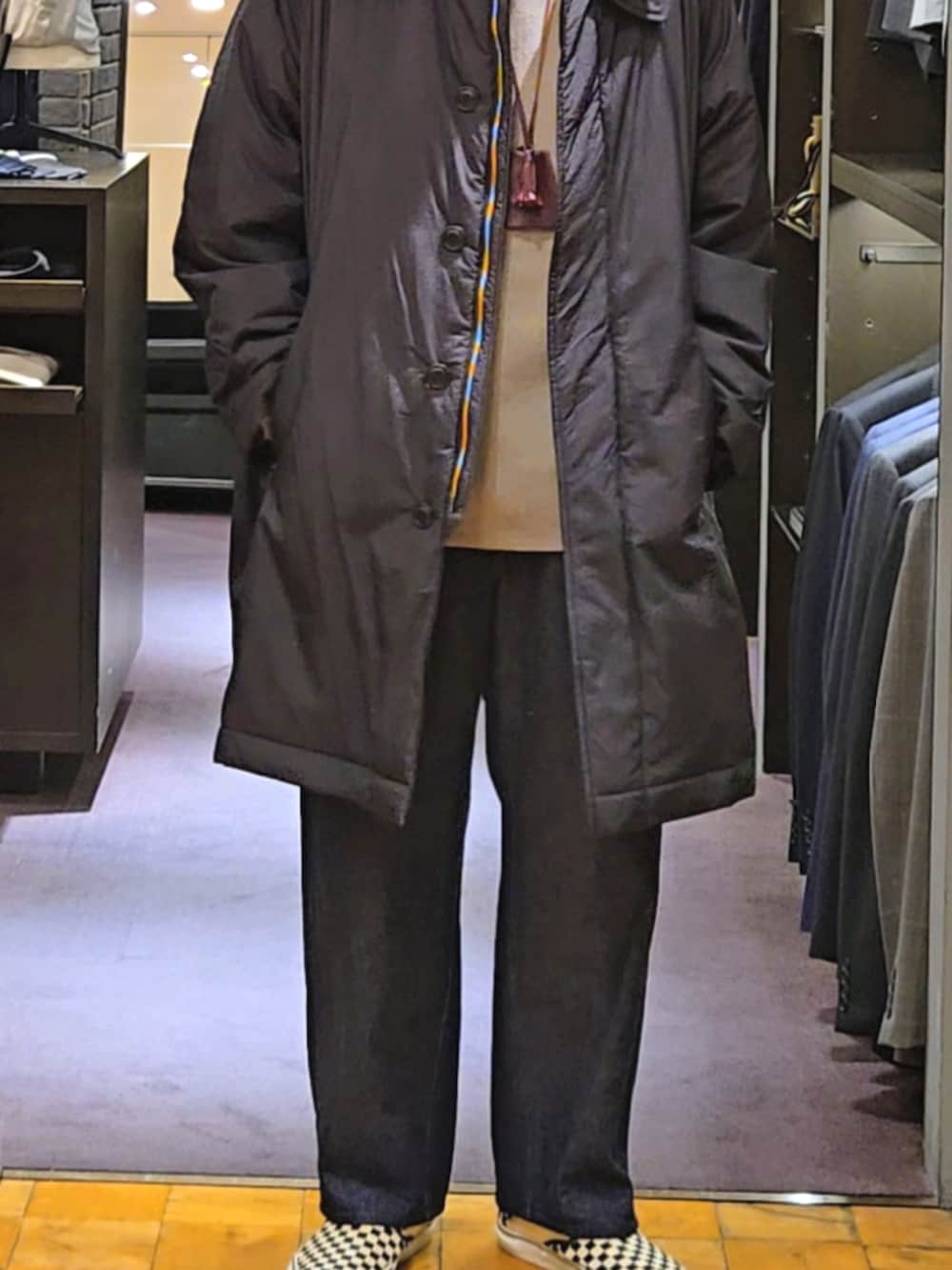 ブラック系のステンカラーコート、ブルー系のデニムパンツ、ベージュ系のニット/セーターを着用したメンズの秋コーディネートの2枚目の写真