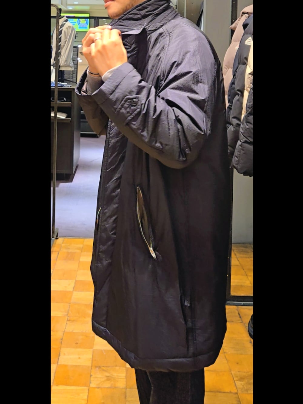 ブラック系のステンカラーコート、ブルー系のデニムパンツ、ベージュ系のニット/セーターを着用したメンズの秋コーディネートの3枚目の写真