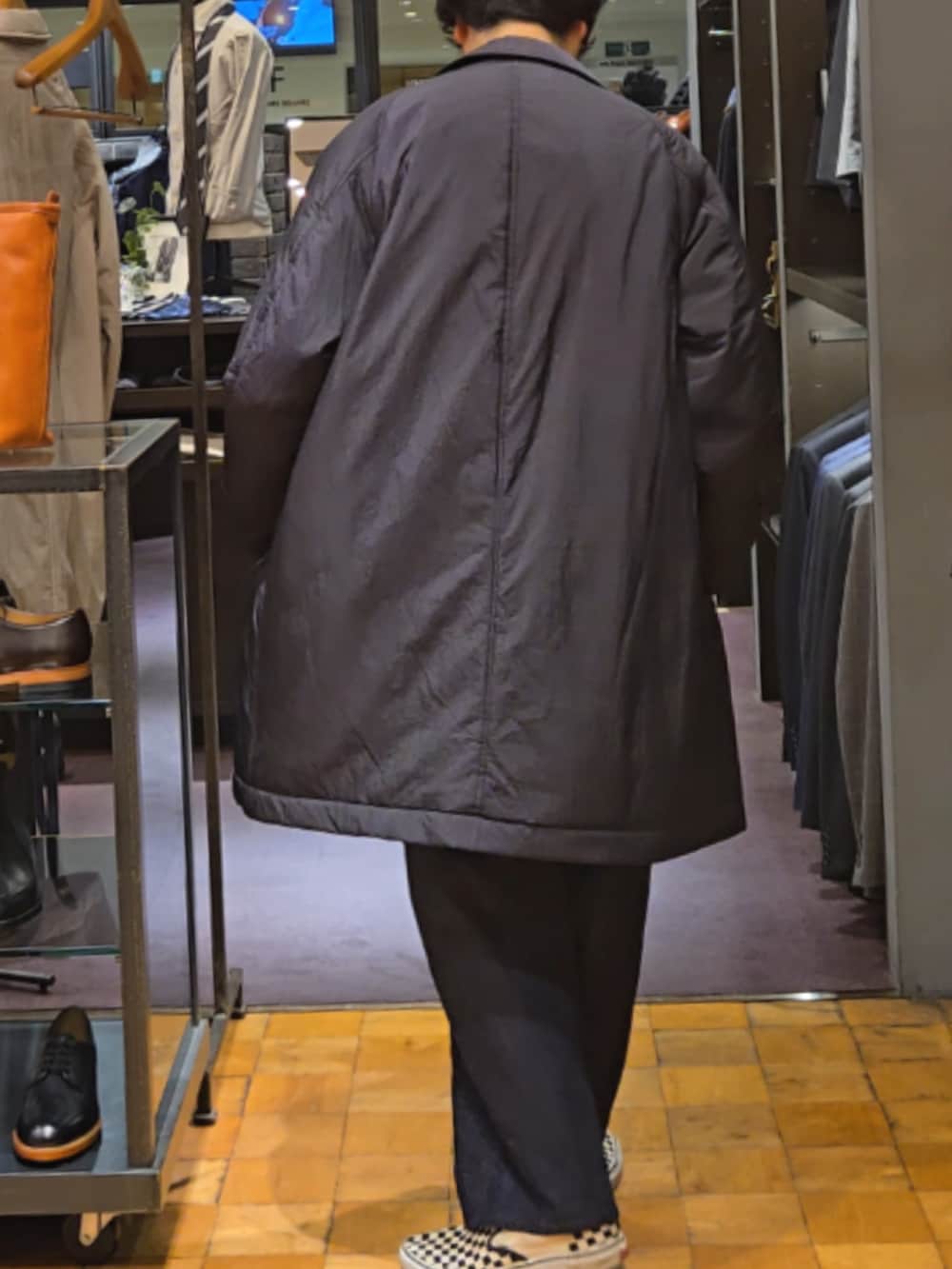 ブラック系のステンカラーコート、ブルー系のデニムパンツ、ベージュ系のニット/セーターを着用したメンズの秋コーディネートの4枚目の写真