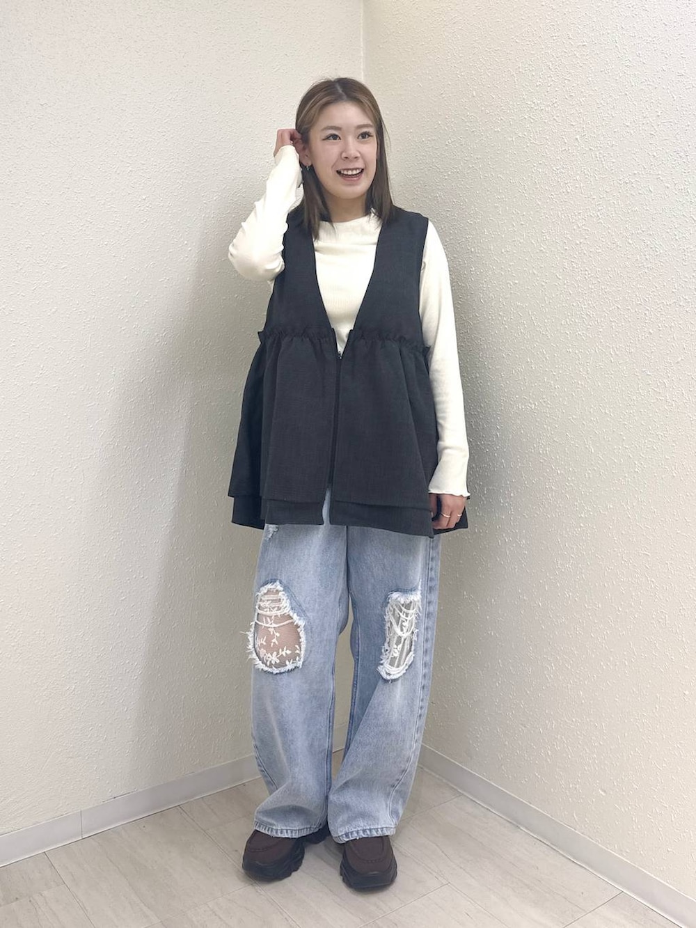 グレー系のベスト、ブルー系のデニムパンツ、ブラウン系のローファーを着用したレディースの冬コーディネートの2枚目の写真