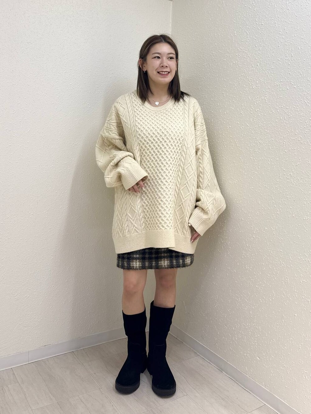 グレー系のスカート、ホワイト系のニット/セーター、ブラック系のブーツを着用したレディースの冬コーディネートの2枚目の写真