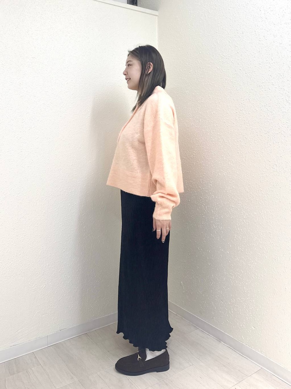 ブラック系のスカート、ピンク系のニット/セーター、ブラウン系のモカシン/デッキシューズを着用したレディースの冬コーディネートの2枚目の写真