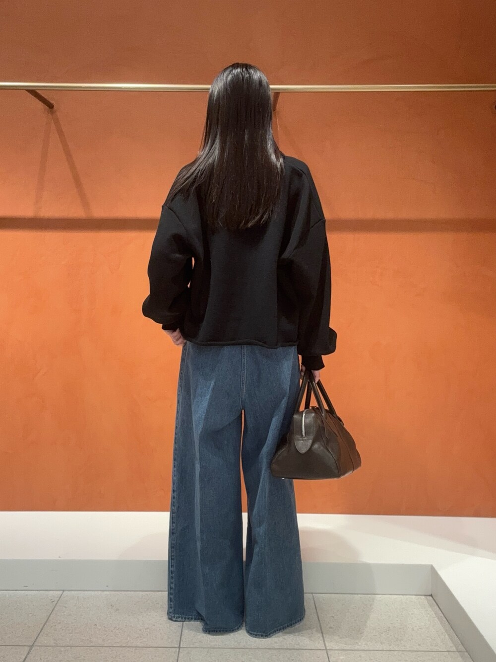 ブラック系のスウェット、ブルー系のデニムパンツ、イエロー系のパンプスを着用したレディースの冬コーディネートの2枚目の写真
