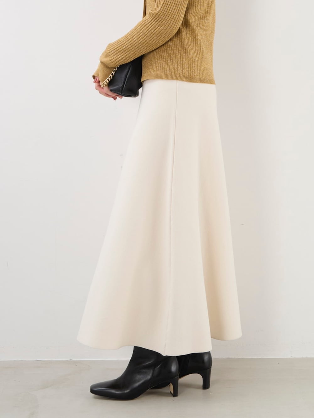 イエロー系のニット/セーター、ブラック系のショルダーバッグ、ホワイト系のスカートを着用したレディースの秋コーディネートの5枚目の写真