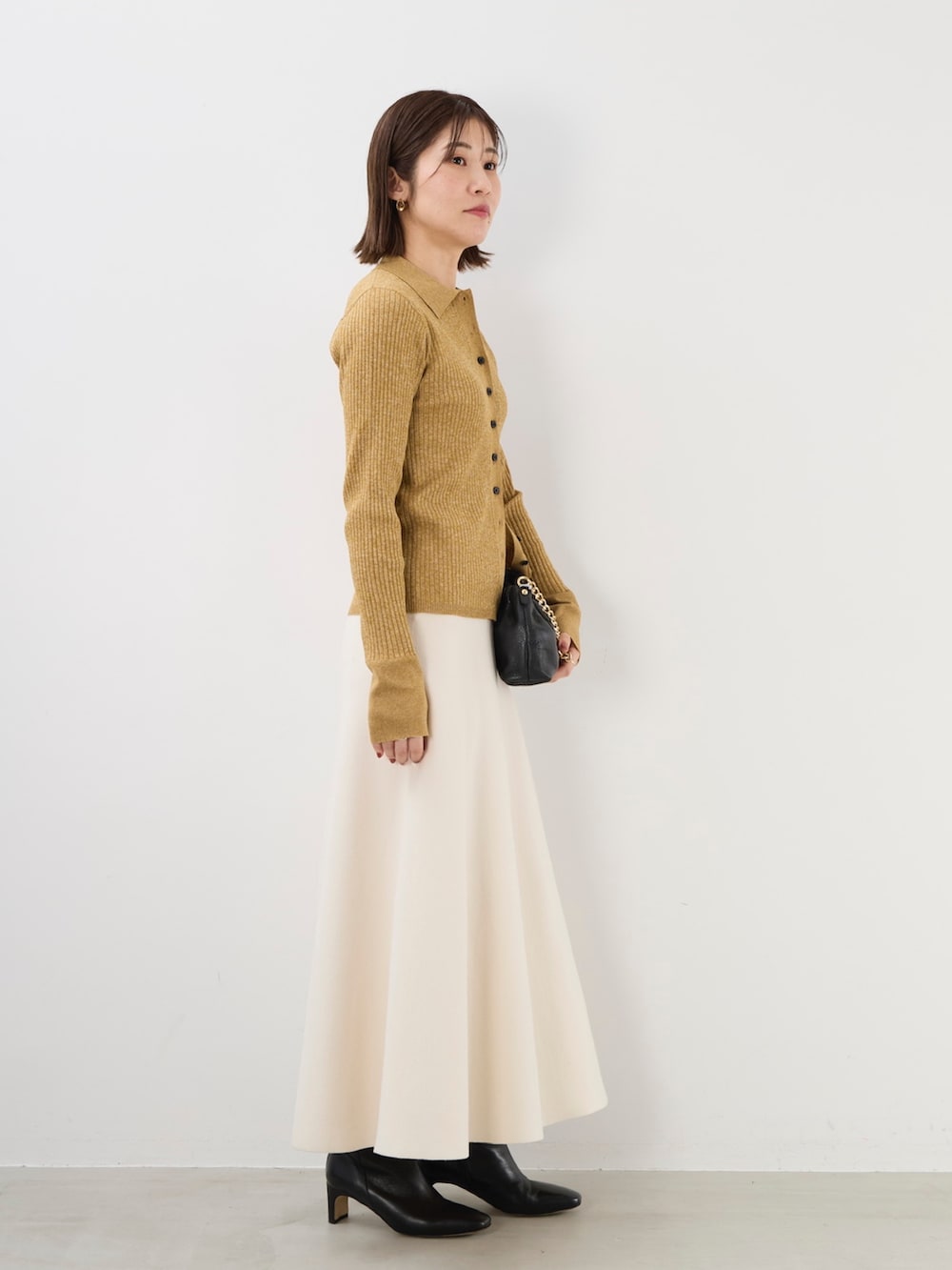 イエロー系のニット/セーター、ブラック系のショルダーバッグ、ホワイト系のスカートを着用したレディースの秋コーディネートの4枚目の写真