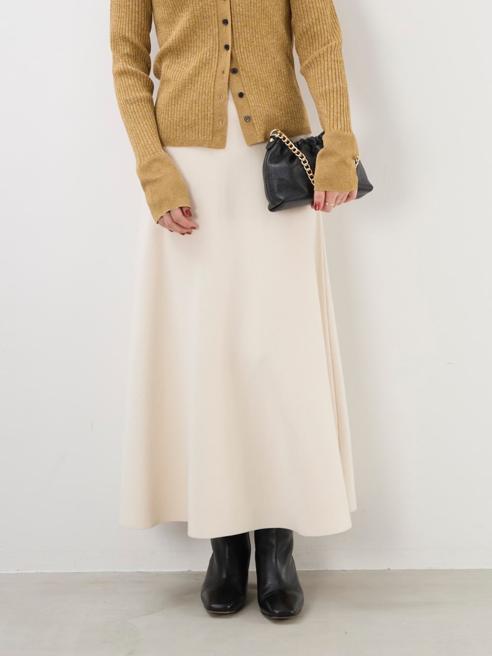 イエロー系のニット/セーター、ブラック系のショルダーバッグ、ホワイト系のスカートを着用したレディースの秋コーディネートの3枚目の写真