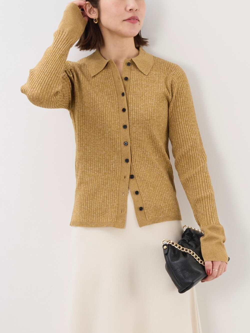 イエロー系のニット/セーター、ブラック系のショルダーバッグ、ホワイト系のスカートを着用したレディースの秋コーディネートの2枚目の写真